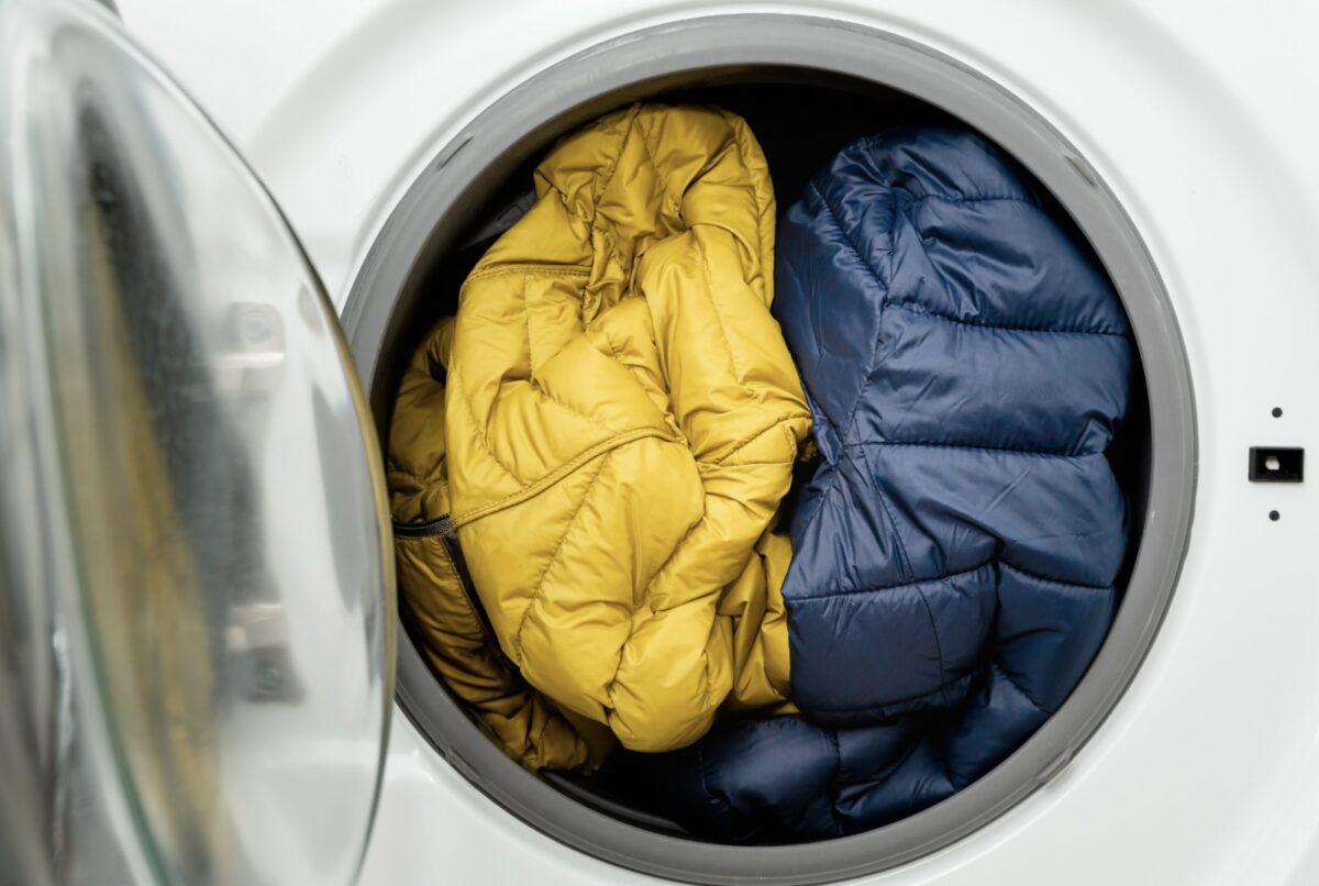 Zwei Daunenjacken (die eine ist blau, die andere ist gelb) liegen in einer Waschmaschine