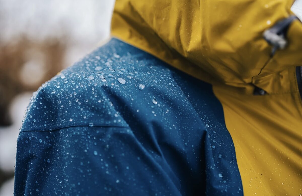 Auf dem Bild ist eine blau-gelbe Regenjacke zu sehen, an der die Regentropfen abprallen.