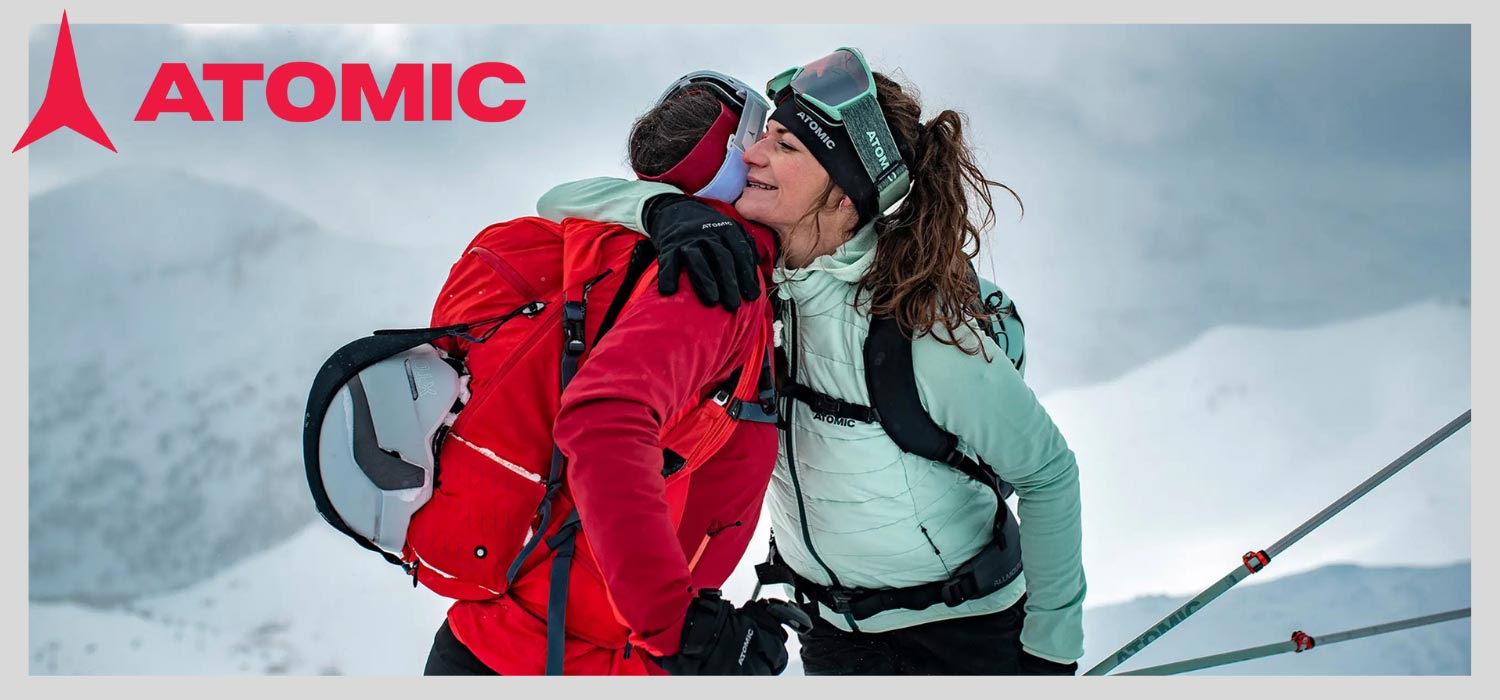 2 Menschen in Winterbekleidung vor Schneekulisse, die sich umarmen